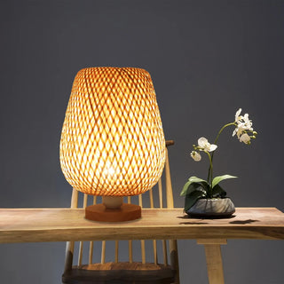 Lampe à poser bois à LED faite à la main posée sur une table avec une chaise et un pot de fleur à droite sur fond gris