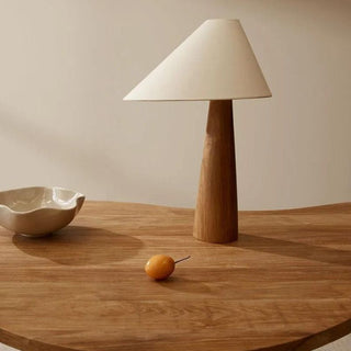 Lampe à poser bois massif pour table avec abat-jour en tissu, posée sur une table en bois aux formes arrondies, à côté d'un vide-poche en céramique blanc et d'un fruit orange.