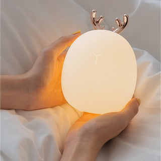 Lampe à poser enfant LED avec cornes de cerf dans les mains d'une personne sur un drap blanc