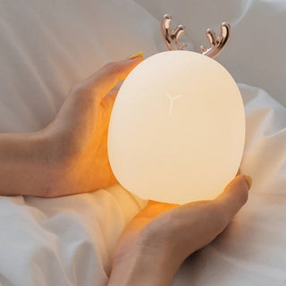 Lampe à poser enfant LED avec cornes de cerf dans les mains d'une personne sur un drap blanc