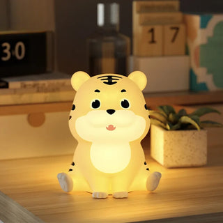 Lampe à poser enfant LED en forme de tigre sur un meuble avec des jouets et une plante verte en fond