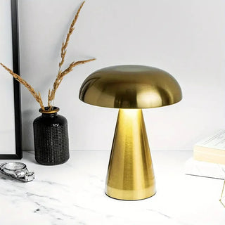 Lampe à poser sans fil LED style champignon doré sur un meuble blanc marbré avec une montre et un pot avec des épis dedans et un livre à droite