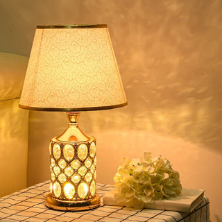 Lampe à poser vintage luxueuse et dorée posée sur une petite table avec une nappe à carreaux et un livre avec des fleurs dessus à droite