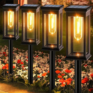 Lot de quatre lampes à poser solaires et automatiques à LED dans un jardin avec de l'herbe et des fleurs blanches et rouges en dessous