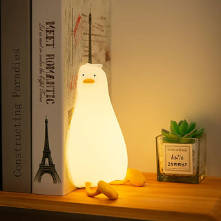 Veilleuse à poser en forme de canard à LED posée sur un meuble avec des livres et un pot de fleur en verre