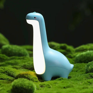 Veilleuse à poser en forme dinosaure mignon, bleu et blanc, allumé, posé sur de la mousse verte synthétique.